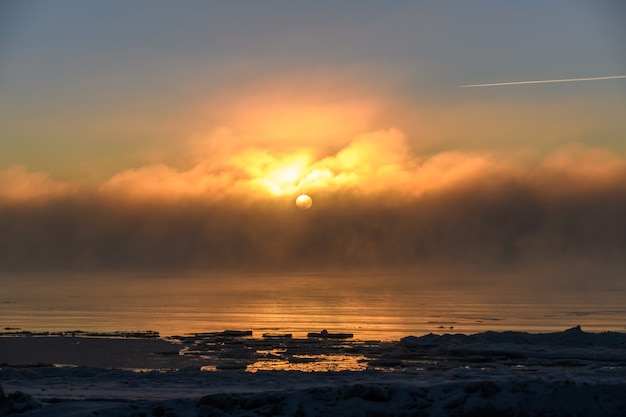 Schöner Sonnenuntergang mit Nebel im arktischen Meer zur Winterzeit. Nebel auf See. Gefrorene Luft.