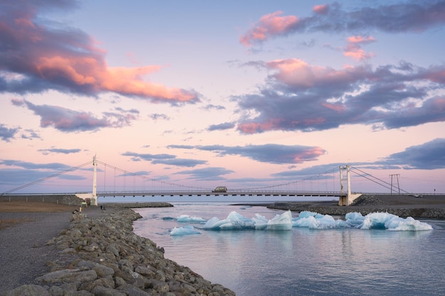 Schöner Sonnenuntergang über der Hängebrücke an der Jokulsarlon-Gletscherflusslagune mit Eisberg, der im Süden des Vatnajokull-Nationalparks in Island schwimmt