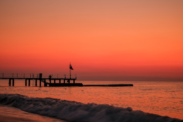 Schöner Sonnenuntergangsonnenaufgangstrand mit rosa Himmel und Pier. Reise-, Entspannungs- und Meditationskonzept