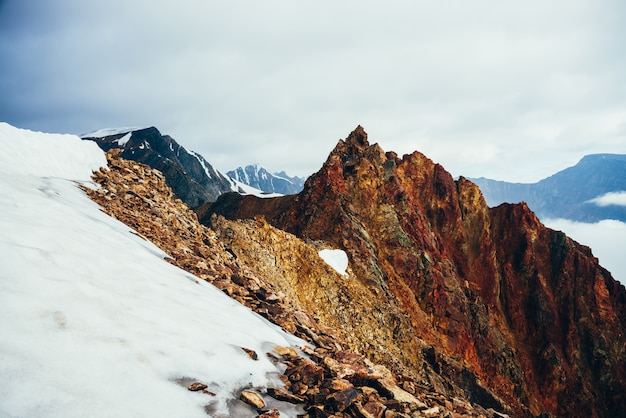 Schöner spitzer Felsgipfel auf riesigem schneebedeckten Berg. Lebhafter großer spitzer felsiger Gipfel. Atmosphärische minimalistische Alpenlandschaft. Scharfer felsiger Berggipfel im bewölkten Himmel. Wunderbare Hochlandlandschaft.