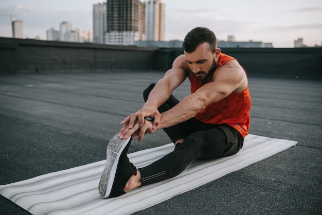 Schöner Sportler, der sich auf einer Yogamatte auf dem Dach dehnt