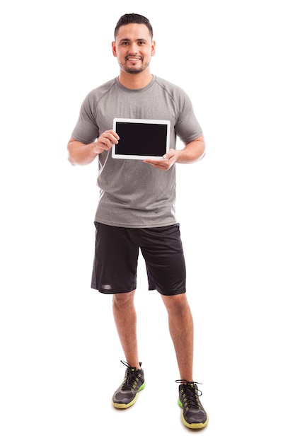 Schöner sportlicher Mann, der den Bildschirm eines Tablet-Computers mit der neuesten Fitness-App zeigt