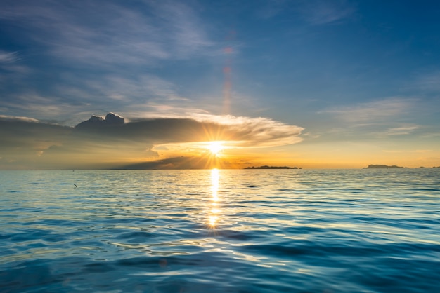 Schöner Strandsonnenuntergang mit blauem Meer und goldenem hellem Himmel bewölken Hintergrund