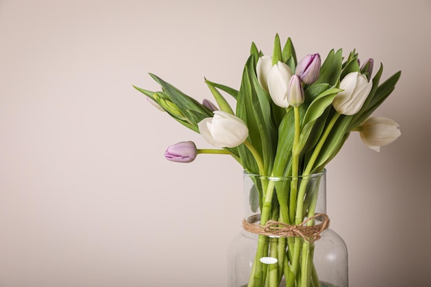 Schöner Strauß bunter Tulpen in Glasvase auf beigem Hintergrund Platz für Text