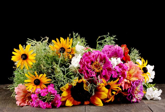 Schöner Strauß heller Blumen auf Holztisch auf schwarzem Hintergrund