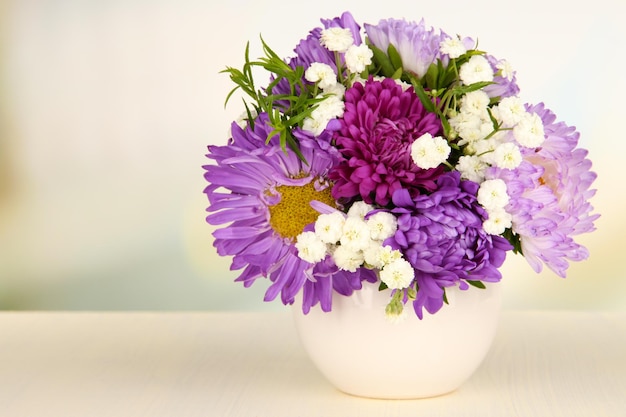 Schöner Strauß heller Blumen in farbiger Vase auf Holztisch auf hellem Hintergrund