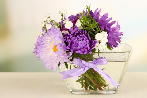 Schöner Strauß heller Blumen in Glasvase auf Holztisch auf hellem Hintergrund