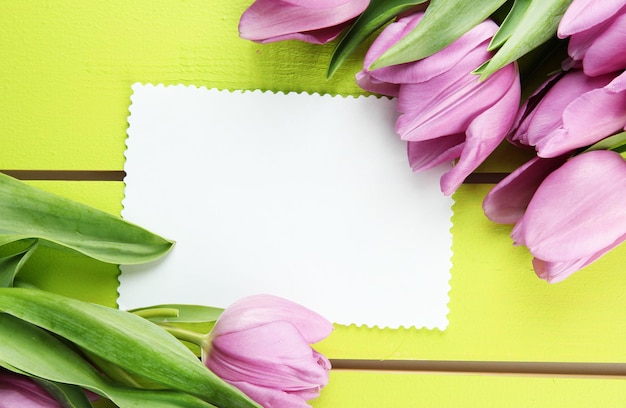 Schöner Strauß lila Tulpen und leere Karte auf grünem Holzhintergrund