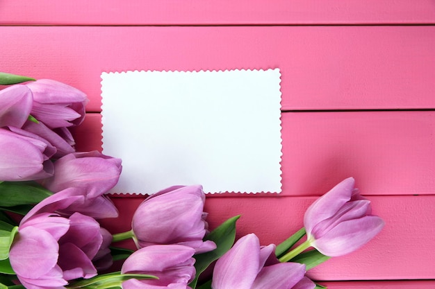 Schöner Strauß lila Tulpen und leere Karte auf rosa Holzhintergrund