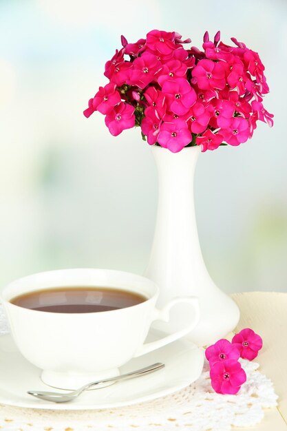 Schöner Strauß Phlox mit Tasse Tee auf dem Tisch auf hellem Hintergrund