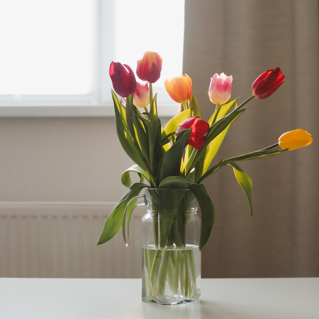 Schöner Strauß Tulpen in Glasvase auf weißem Tisch in einem gemütlichen Zimmer Interieur Blühende Blumendekoration im Wohnzimmer