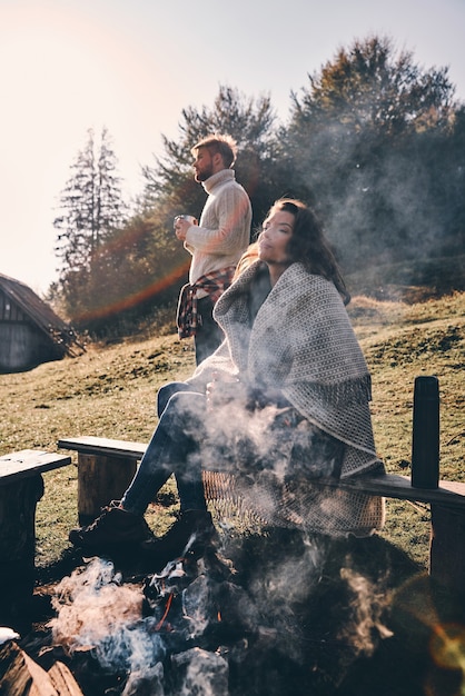 Schöner Tag. Modernes junges Paar beim Morgenkaffee, während es Zeit am Lagerfeuer in den Bergen verbringt