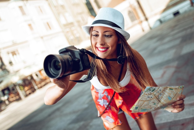 Schöner Tourist des jungen Mädchens, der Karte hält und mit Digitalkamera fotografiert.