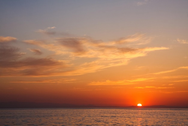 Schöner und farbenfroher Sonnenuntergang, warmes Licht und viele Wolken, Meereswellen an der Meeresküste
