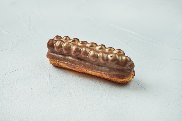 Schöner und leckerer Eclair mit weiß-roter Glasur und gesalzenem Karamellgeschmack auf einer weißen Texturoberfläche. Nahansicht