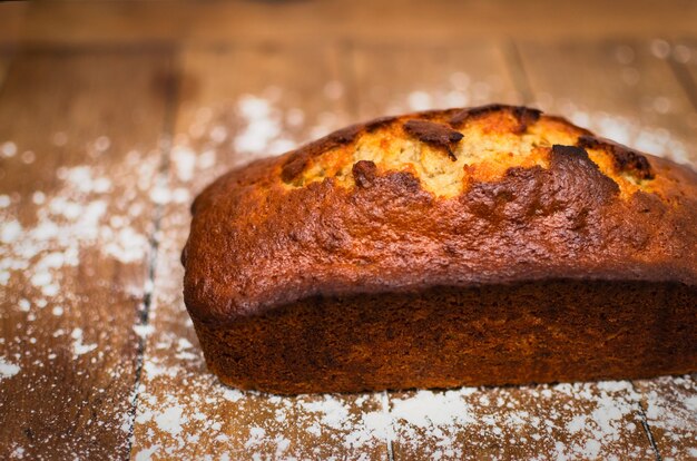 Schöner und leckerer hausgemachter Bananen-Pfund-Kuchen auf Holztisch und Mehl herum