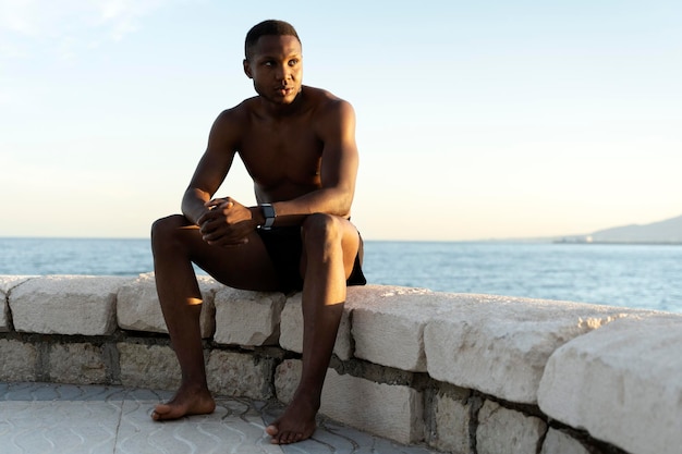 Schöner und selbstbewusster junger Afroamerikaner, der am Strand sitzt