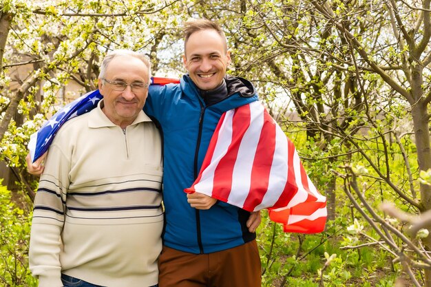 Schöner Vater mit seiner kleinen süßen Sonne liegt auf grünem Rasen auf amerikanischer Flagge mit American-Football-Ball in der Hand.