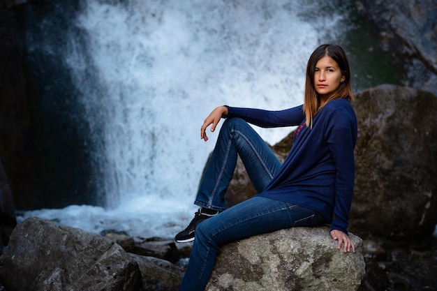 Schöner Wanderer der jungen Frau, der nahe Wasserfall sitzt