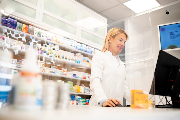 Schöner weiblicher blonder Apotheker, der in Drogerie steht und Medikamente verkauft.