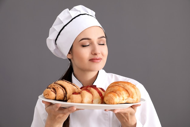 Schöner weiblicher Koch, der Teller mit Croissants auf grauer Oberfläche hält