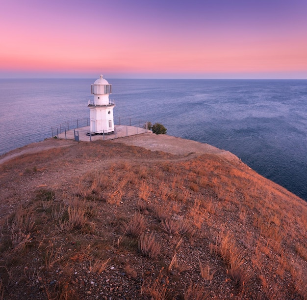 Schöner weißer Leuchtturm an der Küste des Ozeans bei Sonnenuntergang Landschaft