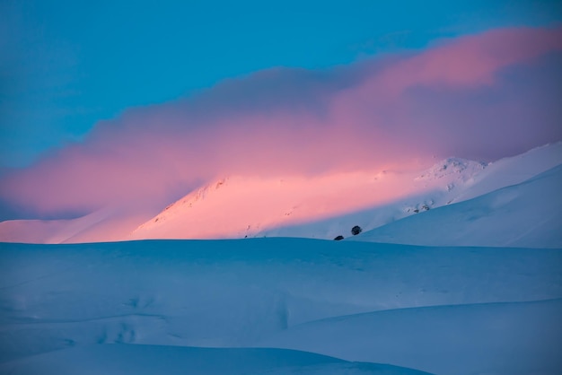 Schöner Wintersonnenuntergang auf Schneehügeln mit rosafarbenen Wolken