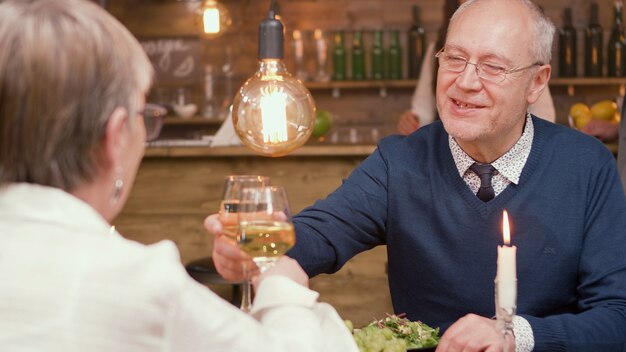 Schönes älteres Ehepaar, das Toast macht und Gläser klirrt. Essen im Restaurant. Mann und Frau in den Sechzigern.