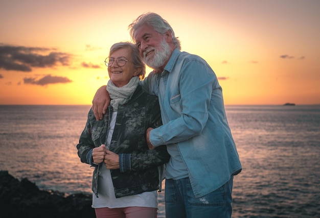 Schönes älteres Paar, das auf den Felsen am Meer steht und die Natur und Freiheit bei Sonnenuntergang genießt Entspannter Lebensstil für ein kaukasisches Paar von Rentnern