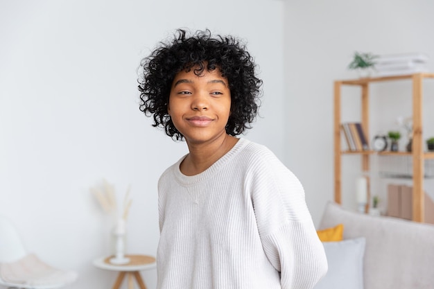 Schönes afrikanisch-amerikanisches Mädchen mit Afro-Frisur zu Hause im Innenbereich Junge afrikanische Frau mit lockigem Haar im Wohnzimmer Beauty ethnische Menschen häusliches Lebenskonzept