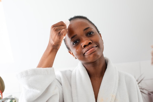 Schönes afrikanisches Mädchen, das Gesicht mit Rosenquarz Gua Sha massiert