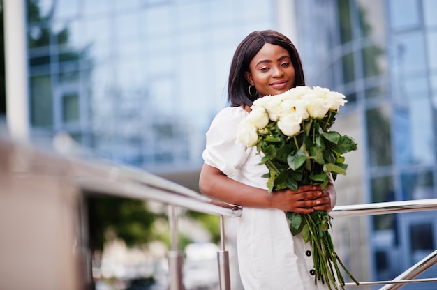 Schönes afroamerikanisches Mädchen in einem weißen Kleid mit Blumen in den Händen