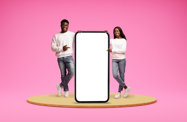 Schönes afroamerikanisches Paar, das auf ein riesiges Telefon zeigt