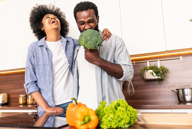 Schönes afroamerikanisches Paar, das zu Hause kocht - Schönes und fröhliches schwarzes Paar, das gemeinsam das Abendessen in der Küche zubereitet