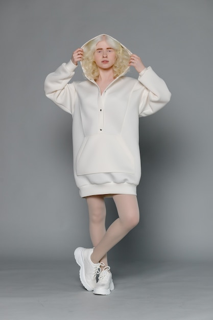 Schönes Albino-Mädchen mit weißer Haut, natürlichen Lippen und weißem lockigem Haar, das einen stylischen weißen Pullover trägt, Nahaufnahmefoto, Kopienraum, Schönheit, Mode. Blondes Mädchen