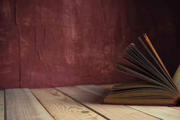 Schönes altes offenes altes Buch auf einem roten Holztisch und dunkler Wandhintergrund dahinter