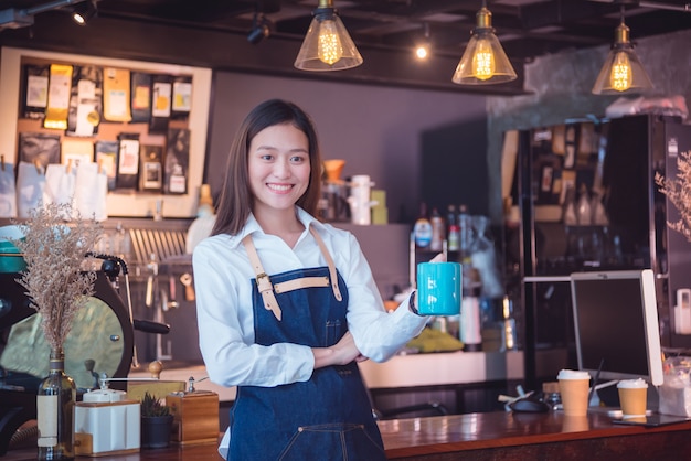 Schönes asiatisches barista, das Kaffeetasse hält und an der Kamera lächelt