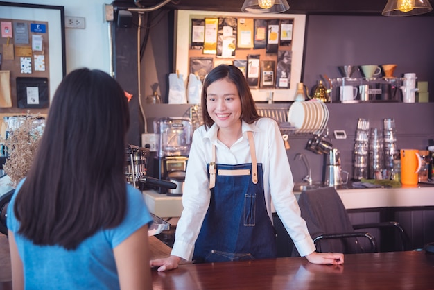 Schönes asiatisches barista, das mit ihrem Kunden und Lächeln in ihrem Café spricht