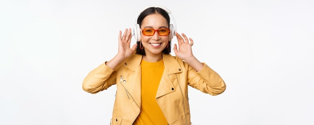 Schönes asiatisches Mädchen, das glückliche hörende Musik in den Kopfhörern lacht, die über weißem Hintergrund stehen