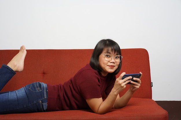 Schönes asiatisches Mädchen, das rotes Hemd und blaue Jeans trägt, spielt Handyspiel auf dem Smartphone