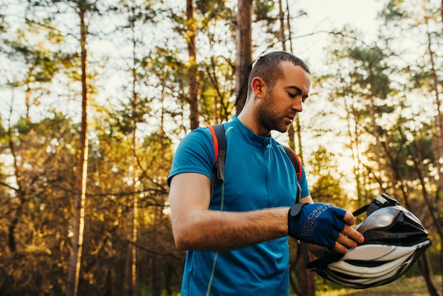 Schönes Außenporträt von gut aussehenden bärtigen männlichen Radfahrern mit Schutzausrüstung vor dem Rennen, das auf der Straße vor grünem Baumhintergrund steht Reisekonzept Sport-Lifestyle