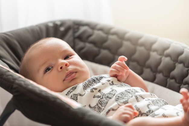 Schönes Baby, das an der Kamera in hintergrundbeleuchtetem weichem Licht liegt und aufpasst