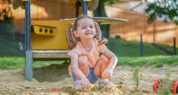 Schönes Baby, das sich an einem sonnigen, warmen Sommertag amüsiert Süßes Kleinkind, das im Sand auf dem Spielplatz im Freien spielt