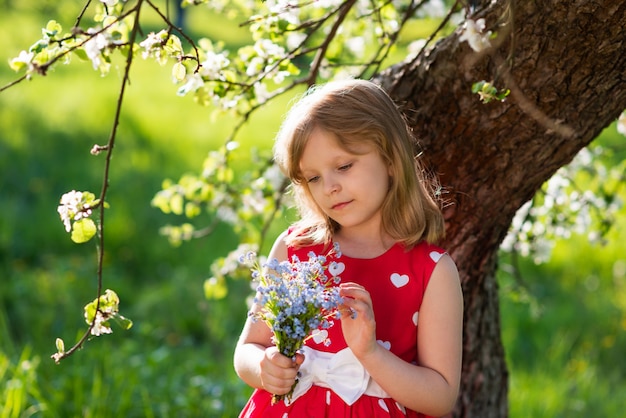 Schönes Baby, das unter einem Baum mit einem Blumenstrauß von Wildblumen in ihren Händen sitzt