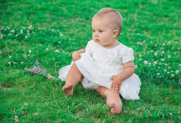 Schönes Baby im weißen Kleid, das auf dem Rasen sitzt