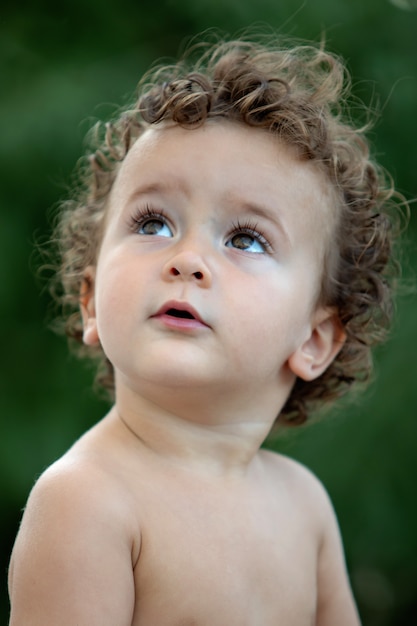 Schönes Baby mit dem lockigen Haar im Garten