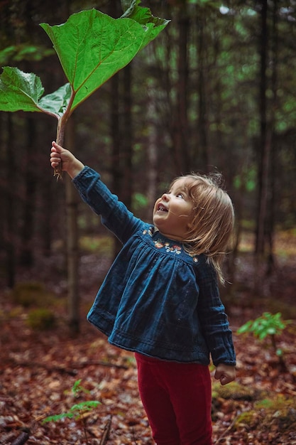 Schönes Baby versteckt sich im Wald vor dem Regen unter der Klette