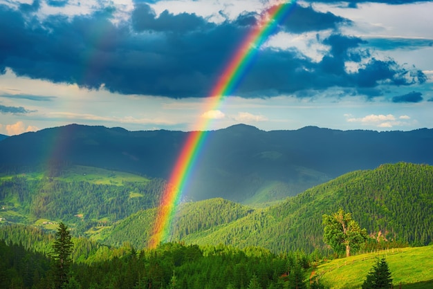 Schönes Bergtal mit grünen Hügeln und riesigem Regenbogen im Sommer. Natürlicher Reisehintergrund im Freien. Karpaten, Ukraine