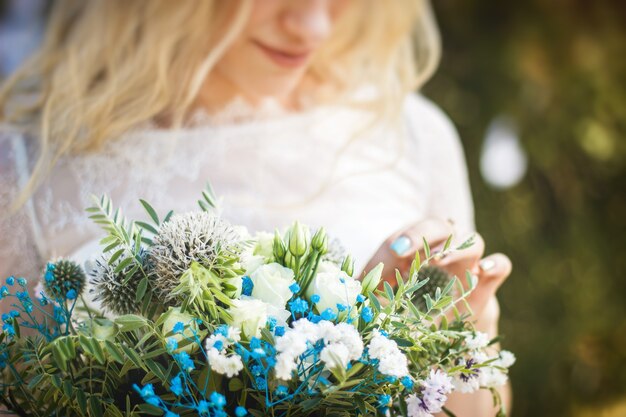 Schönes blondes Brautporträt mit Blumenstrauß und Kranz auf ihrem Kopf im weißen Hochzeitskleid