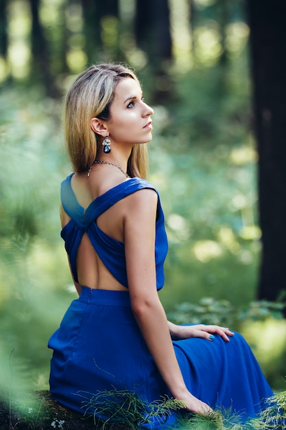 Schönes blondes langes blaues Kleid allein im Wald